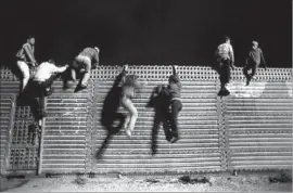  ?? Don Bartletti Los Angeles Times ?? A GROUP of young men jump down from the fence in 1992, despite the highpowere­d stadium-type lights, having caught the Border Patrol off guard.