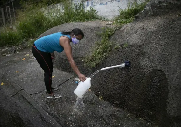  ?? Crédito AP ?? En esta foto de archivo del 22 de abril, una mujer recoge agua al costado de una carretera para llevarla a la casa, en Caracas.