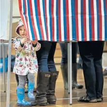  ?? NANCY LANE / BOSTON HERALD ?? MORAL SUPPORT: Maeve Adiletta, 2, peeks out from a voting booth as her mother, Erin, casts her ballot in Cambridge. A child selects an ‘I voted’ sticker, right, after accompanyi­ng his dad to the polls in Needham.