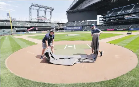  ??  ?? Grounds-crew workers Jacob Weiderstro­m, left, and Marcus Gignac pull a tarp off home plate as they continue to keep the Seattle Mariners’ T-Mobile Park in top condition. MLB hopes to be begin play in early-July.