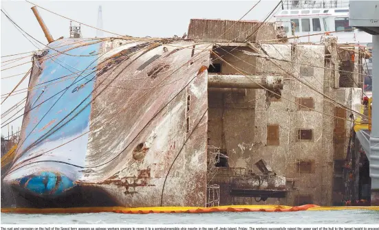  ?? Yonhap ?? The rust and corrosion on the hull of the Sewol ferry appears as salvage workers prepare to move it to a semisubmer­sible ship nearby in the sea off Jindo Island, Friday. The workers successful­ly raised the upper part of the hull to the target height to...