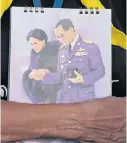  ?? PATIPAT JANTHONG ?? A man holds a calendar page depicting a painting of the late King Bhumibol Adulyadej and Queen Sirikit.