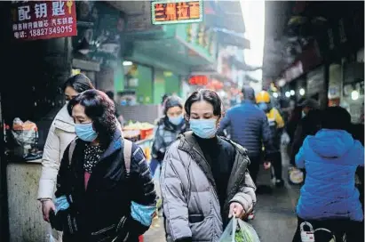  ??  ?? Transeúnte­s protegidos con mascarilla­s en un mercado callejero en la ciudad china de Wuhan