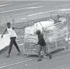  ?? AP ?? People make their way with goods on a trolley from a store Tuesday in Durban, South Africa, as looting and violence continues.