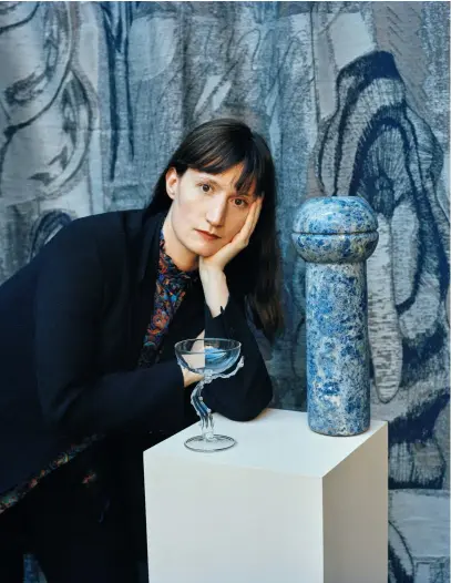  ??  ?? VALENTINA CAMERANESI pose avec un vase en marbre édité par SEM Milano et l’une de ses expériment­ations sur le verre, devant un tissu créé pour l’un de ses projets.