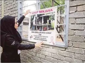  ?? BERNAMA PIC ?? (Left) Cancer Survivors Malaysia founder Zuraini Kamal putting a ‘Projek Hidup Berjasa’ banner on a new house being built for a needy family in Kampung Teluk Chengal near Alor Star on Saturday.