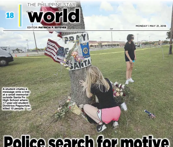  ?? AFP ?? A student chalks a message onto a tree at a small memorial outside Santa Fe High School where 17-year-old student Dimitrios Pagourtzis killed 10 people.