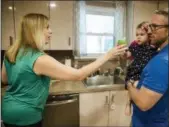  ?? ASSOCIATED PRESS ?? Lauren Woehr hands her 16-monthold daughter Caroline, held by her husband Dan McDowell, a cup filled with bottled water at their home in Horsham.