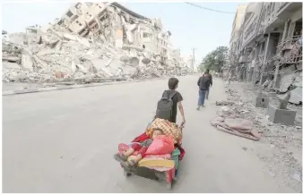  ?? — Reuters ?? A Palestinia­n boy pulls a cart carrying his brother and their belongings as they flee their home during Israeli air and artillery strikes, near the site of a tower building destroyed in earlier strikes in Gaza City.