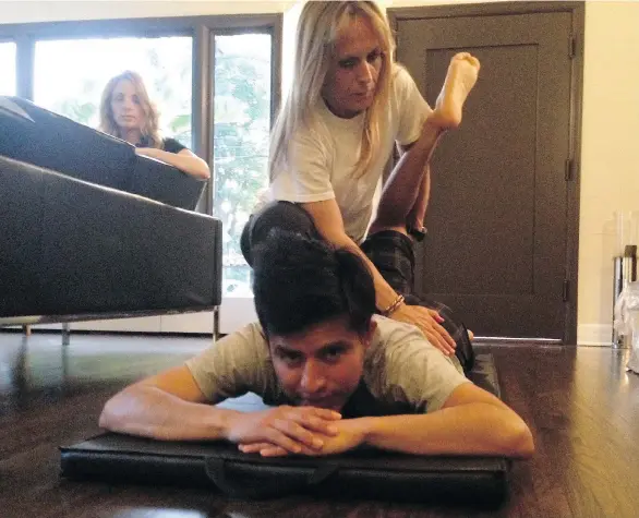  ?? DENISE RYAN ?? Jockey Mario Gutierrez works on stretching with fitness coach Sabrina Perruzi as his wife Rebecca looks on in their home. He’s now in the top 10 in U.S. jockey rankings.