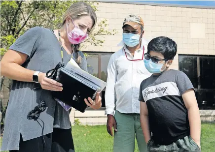  ?? [COURTNEY HERGESHEIM­ER/DISPATCH] ?? Beth Uhlenhake, a school counselor, hands instructio­ns and a Chromebook to Padam Subedi and his son Anish, who is starting eighth grade at Slate Ridge Elementary, on Friday. Reynoldsbu­rg is starting the year online.