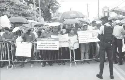  ??  ?? An officer looks on as protestors congregate­d at the barrier closest to GECOM’s headquarte­rs. (Photo by Terrence Thompson)