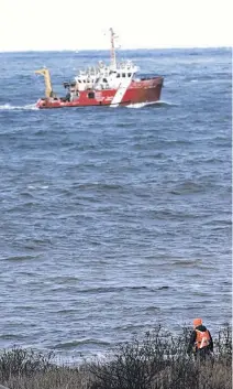  ?? TIM KROCHAK • THE CHRONICLE HERALD ?? A searcher looks on near Parkers Cove, Annapolis County, as the Canadian Coast Guard ship M. Perley conducts a search for missing fishermen.