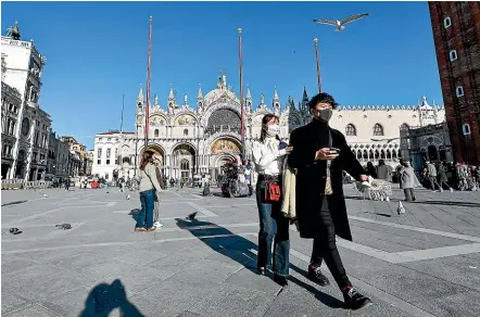  ?? AP ?? Tourists wearing face masks as protection against the coronaviru­s outbreak walk through the normally crowded St Mark’s Square in Venice yesterday. Authoritie­s in Italy – which has the most coronaviru­s cases outside Asia – have decided to reopen schools and museums in some of the less hard-hit areas.