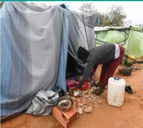  ?? AFP PIC ?? A migrant from Sub-Saharian Africa preparing food in front of a tent at a camp in Jebeniana in Tunisia’s Sfax governorat­e last Wednesday.