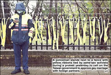  ?? AFP ?? A policeman stands next to a fence with yellow ribbons tied by same-sex activists during a protest yesterday to call on the Taiwan government to approve gay marriage with foreign partners.