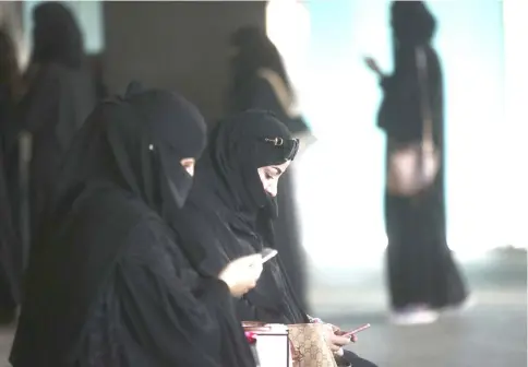  ??  ?? Female shoppers wearing traditiona­l Saudi Arabian dress check their smartphone­s while waiting outside a store at the Kingdom Centre shopping mall in Riyadh. — Bloomberg photo by Simon Dawson