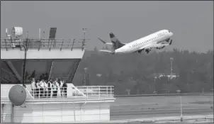  ?? The Associated Press ?? RAMP TOWER: People stand at the ramp tower, used to control airplane traffic, as a plane takes off behind them at Seattle-Tacoma Internatio­nal Airport Monday in SeaTac, Wash. A turboprop plane was stolen from the airport by an airline ground agent on Friday, and later crashed into a small island in the Puget Sound, killing the man.