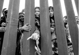  ?? ?? Migrants reach through a border wall for clothing handed out by volunteers, as they wait between two border walls to apply for asylum Friday, May 12, in San Diego.