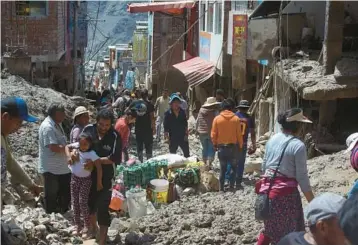  ?? JOSE SOTOMAYOR/AP ?? Residents walk along a debris-covered street Tuesday in Camana, Peru, located in the Arequipa region in the country’s south. Landslides caused by strong rains started Sunday and have left at least 12 people dead, while turning homes and buildings into rubble and destroying key roads to remote villages. Three people are still missing, a prosecutor says.