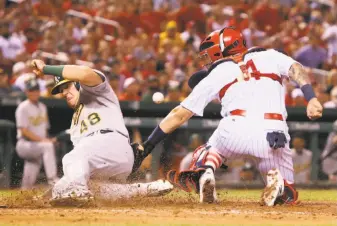  ?? Chris Lee / St. Louis Post-Dispatch ?? Ryon Healy, who had doubled to extend his hitting streak to 13 games, slides past Cardinals catcher Yadier Molina to score the go-ahead run on a sacrifice fly in the eighth inning.