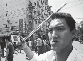  ?? NG HAN GUAN THE ASSOCIATED PRESS ?? July 7, 2009: A Han Chinese man carries a spiked steel bar while using his cellphone to take photos as he joins a mob of Han Chinese men attacking Uighur properties in the aftermath of attacks by the Uighurs in Urumqi, in western China's Xinjiang province.