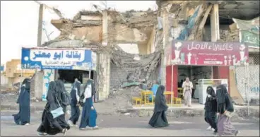  ?? NYT/FILE ?? People walk past the ruins of buildings destroyed in airstrikes on the Old City of Sanaa, Yemen.
