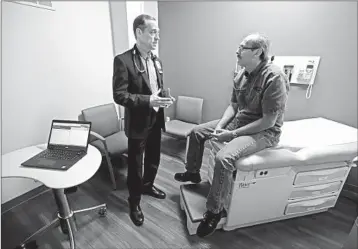  ?? MICHAEL CONROY/AP ?? Dr. John Lynch meets with patient Jeff Thieke during his visit to the Fiat Chrysler Automotive Clinic in Anderson, Ind.