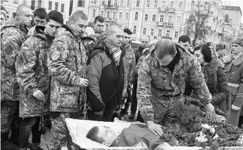  ?? SERGEI SUPINSKY / AFP / GETTY IMAGES ?? A serviceman places carnations on the coffin of Kirill Geintz, 28, a late member of a Ukrainian volunteer battalion,
during his funeral in Kyiv on Feb. 12. There is a newfound spirit of volunteeri­sm in the country, observers say.