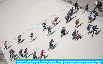  ?? —AFP ?? TIJUANA: A group of Central American migrants -mostly from Honduras- cross the almost dry riverbed of the Tijuana River in an attempt to get to El Chaparral port of entry, in Tijuana, Baja California State, Mexico, near US-Mexico border.