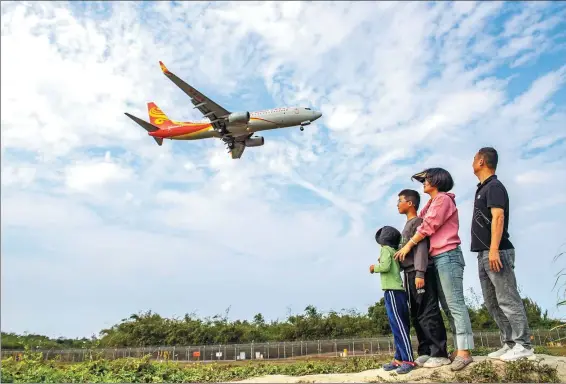  ?? YUAN JINGZHI / FOR CHINA DAILY ?? A family watch a passenger plane outside Haikou Meilan Internatio­nal Airport in Haikou, Hainan province, on Feb 18.