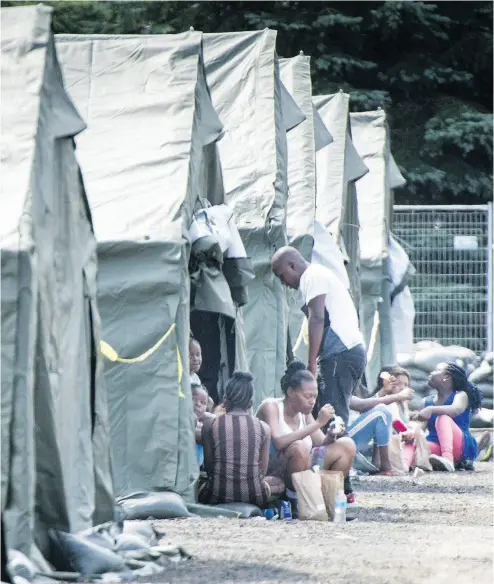  ?? PAUL CHIASSON / THE CANADIAN PRESS FILES ?? Asylum seekers sit in front of their tents in a temporary camp last August near Saint-Bernard-de-Lacolle, Que.
