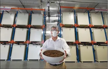  ?? (AP/Ted S. Warren) ?? Micah Truman, CEO of Return Home, a company that composts human remains into soil, poses for a photo Wednesday in Auburn, Wash., south of Seattle. Truman is holding a container of soil made with animal remains that is used to show what the product of their process looks like. Behind him are the metal vessels where bodies are kept during the first month of the two-month composing process.