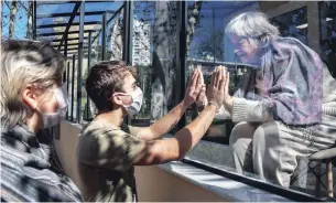  ?? NELSON ALMEIDA AFP/GETTY IMAGES ?? Brazilian Alexandre Schleier, centre, speaks with his 81-year-old grandmothe­r Olivia Schleier through a window at the Premier Hospital in Sao Paulo, Brazil, on Thursday.