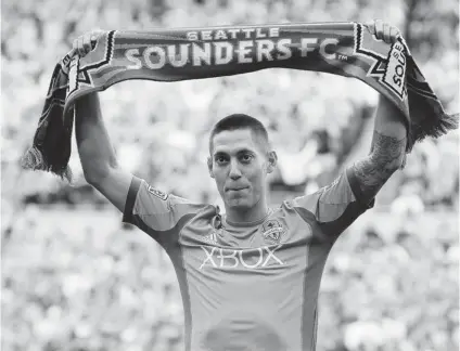  ?? TED S. WARREN/ THE ASSOCIATED PRESS ?? Clint Dempsey, captain of the U. S. men’s national soccer team, raises a Seattle Sounders scarf during a ceremony to introduce him as the newest member of the MLS team on Saturday. Dempsey previously played for Tottenham Hotspur in the English Premier...