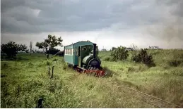  ??  ?? Under lowering skies – a reminder of why so many holidaymak­ers deserted British resorts for Spanish sunshine – Peckett 0-6-0ST Jurassic heads towards the stations at Beach and Fitties camp in 1970. (Trevor Dodgson)