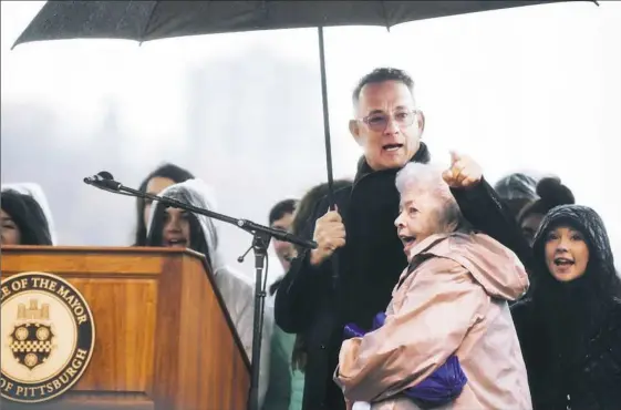  ?? Alexandra Wimley/Post-Gazette ?? Actor Tom Hanks embraces Joanne Rogers, wife of the late Fred Rogers, on Friday as they sing the theme song from “Mister Rogers’ Neighborho­od” with a choir during the Rally for Peace and Tree of Life Victims at Point State Park.