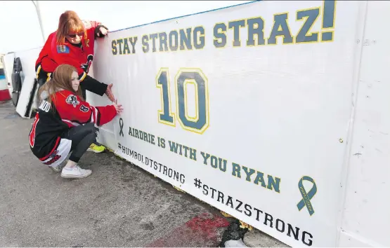  ?? JIM WELLS ?? Tracey Shea, standing, and Taya Nelson ready a sign along the boards in Airdrie during a vigil for local hockey player Ryan Straschnit­zki, who was paralyzed in the Humboldt crash.