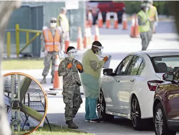  ?? DAVID SANTIAGO dsantiago@miamiheral­d.com ?? A healthcare worker checks in a patient with help from the Florida Army National Guard as vehicles line up at the COVID-19 drive-thru testing center at Marlins Park on Wednesday in Little Havana.