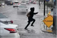  ?? AP PHOTO BY JAMES QUIGG ?? A pedestrian leaps across a flooded portion of the La Paz and Seventh Street intersecti­on as a winter storm arrived, Thursday, Dec. 6, in Victorvill­e, Calif.