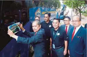  ?? PIC BY MOHD FADLI HAMZAH ?? National Registrati­on Department director-general Datuk Mohamad Razin Abdullah pasting a sticker on the National Registrati­on Department bus for mobile services in Putrajaya yesterday.