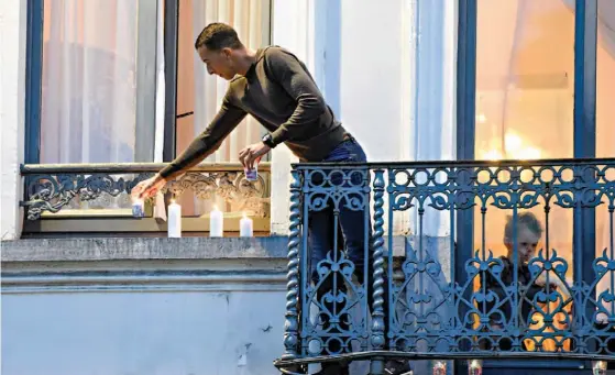  ??  ?? Mohammed Abdeslam, irmão de um dos suicidas de Paris e do suspeito Salah, coloca velas na sua varanda, em Molenbeek, numa homenagem às vítimas dos atentados