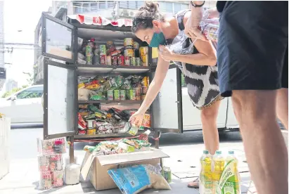  ?? WICHAN CHAROENKIA­TPAKUL ?? A woman adds an item to a community pantry on Sukhumvit Soi 71 in Bangkok. The roadside stall, featuring items such as instant noodles, canned food and basic medicine, was set up by a group called “It Noi” (small brick). Similar pantries have gone up at other locations around Bangkok and in the provinces. The idea has also been adopted in other countries as a way to help people who have lost their income during the Covid-19 lockdown.