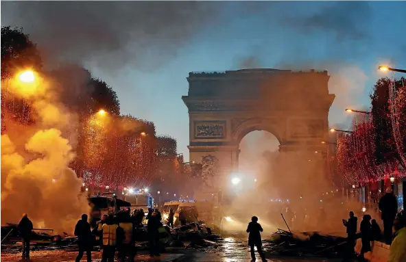  ?? AP ?? Plumes of smoke are seen near the Arc de Triomphe on the Champs-Elysees avenue, which is decorated with the Christmas lights, during a tax protest.