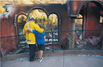  ?? / AP FOTO ?? WILDFIRE. Firefighte­r Terry Sanders and son Isaac, 11, who lost their home in a wildfire, comfort each other in front of their neighbor’s home destroyed by the same wildfire after trying to find sentimenta­l items belonging to the neighbor Saturday, in...