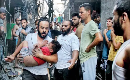  ?? ?? A Palestinia­n man rushes past rubble carrying a child in his arms, following an Israeli military strike on Gaza. AFP