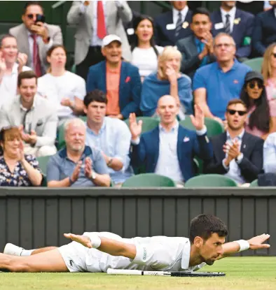  ?? SEBASTIEN BOZON/AFP-GETTY ?? Novak Djokovic reacts after hitting a winner while sliding to the ground during his victory Tuesday at Wimbledon.