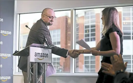  ?? Jessie Wardarski/Post-Gazette ?? Bill Kaper, general manager of Amazon’s Pittsburgh office, shakes hands with Melissa Horvath as she takes the podium to speak during a news conference at the company's South Side offices on Thursday. Ms. Horvath, the owner of Sewickley-based Sweet...