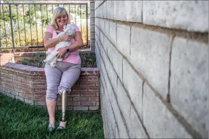  ?? Michele Lutes/The Signal ?? Kathy Willhide-Michiulis smiles as she picks up her dog and enjoys a summer day. Willhide-Michiulis was involved in an incident at a ski resort that took her leg. She has been embroiled in a legal battle with the operators of the ski resort for seven years.