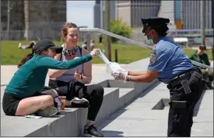  ?? The Associated Press ?? SAFETY OFFICER: New York Police Department School Safety officer Bynoe, right, hands out face masks to women at Brooklyn Bridge Park during the coronaviru­s pandemic Sunday in New York.